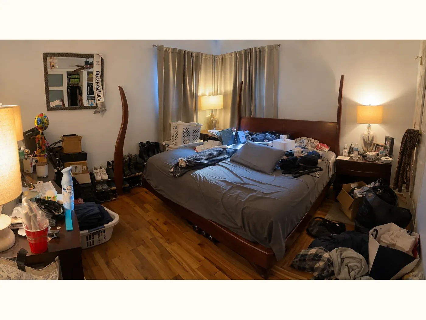 Primary bedroom before organizing — unmade bed covered in clothing, laundry baskets, boxes and clutter on every surface