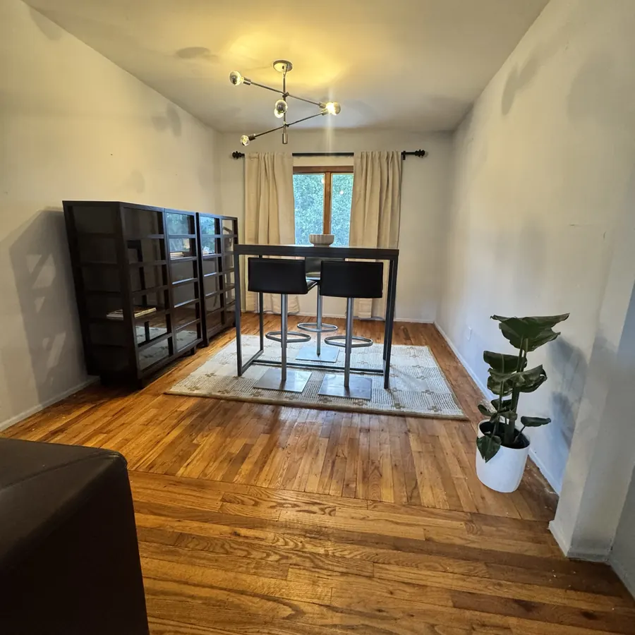 Cleared dining room with hardwood floors, a pendant light, and a single potted plant by the window